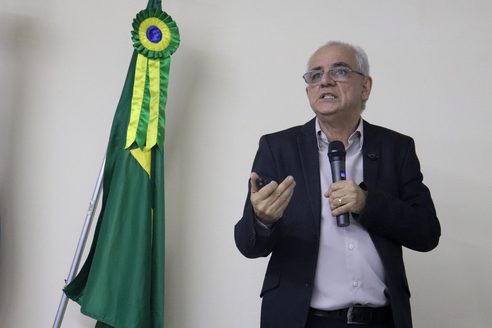 Alexandre Kaiê no palco, com microfone, ao lado da bandeira do Brasil